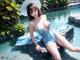 A woman in a blue bathing suit and hat sitting on a rock in a pool.