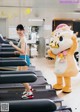 A woman running on a treadmill next to a mascot.